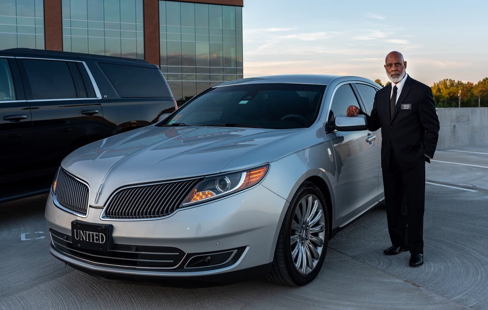 Professional chauffeur in a suit beside a luxury car in the city