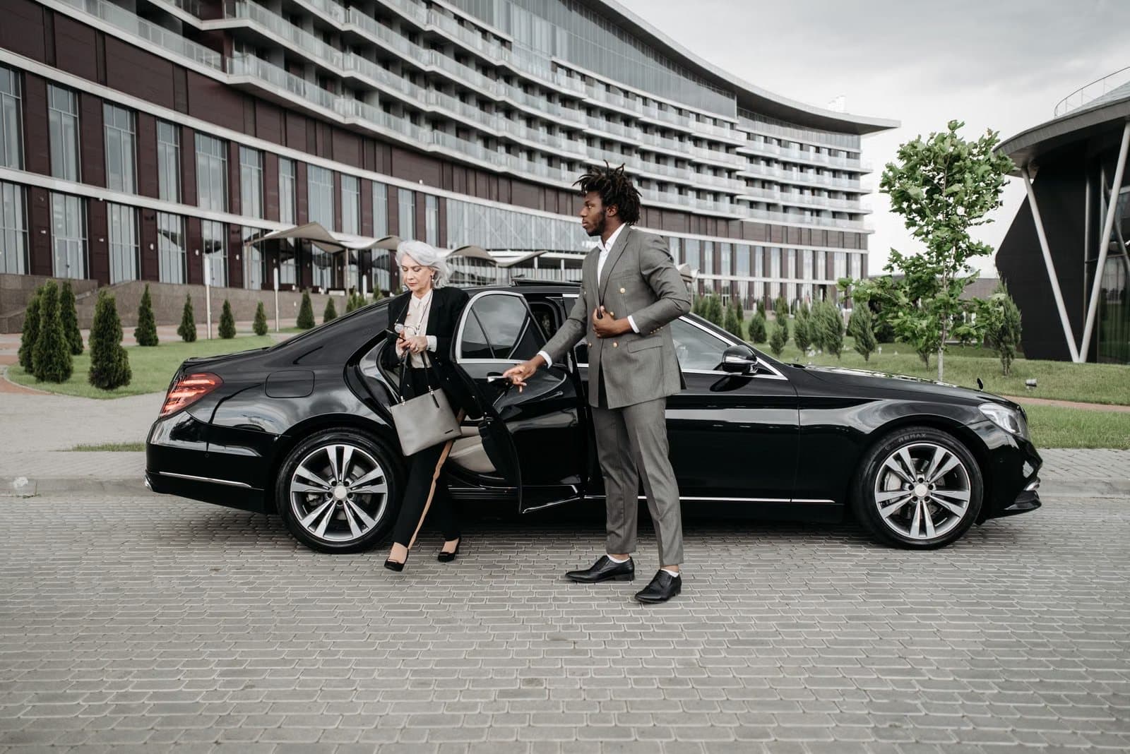 Professional chauffeur helping a business traveller out of a luxury car