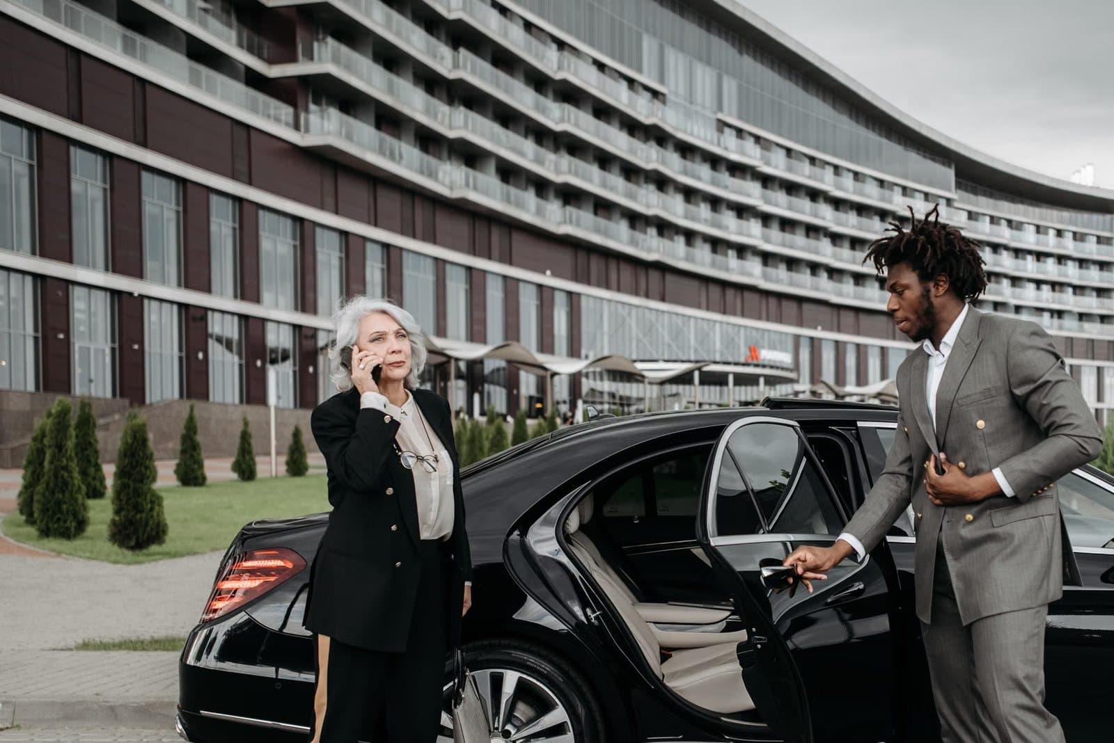Executive on the phone while a chauffeur holds the door of a luxury car